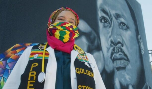 A person in colorful clothing in front of a mural of Martin Luther King Jr.
