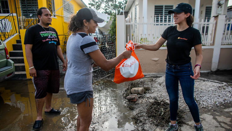 A Direct Relief staff person hands an orange bag of hygiene supplies to a person following Hurricane Fiona.